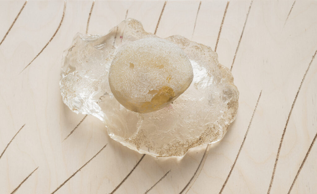 Two cast glass stones displayed on a sheet of engraved timber.